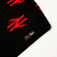 Close-up of a black knit beanie with bold red geometric logo patterns and a small black brand tag reading 'BROKEN PATTERN' on a white background.