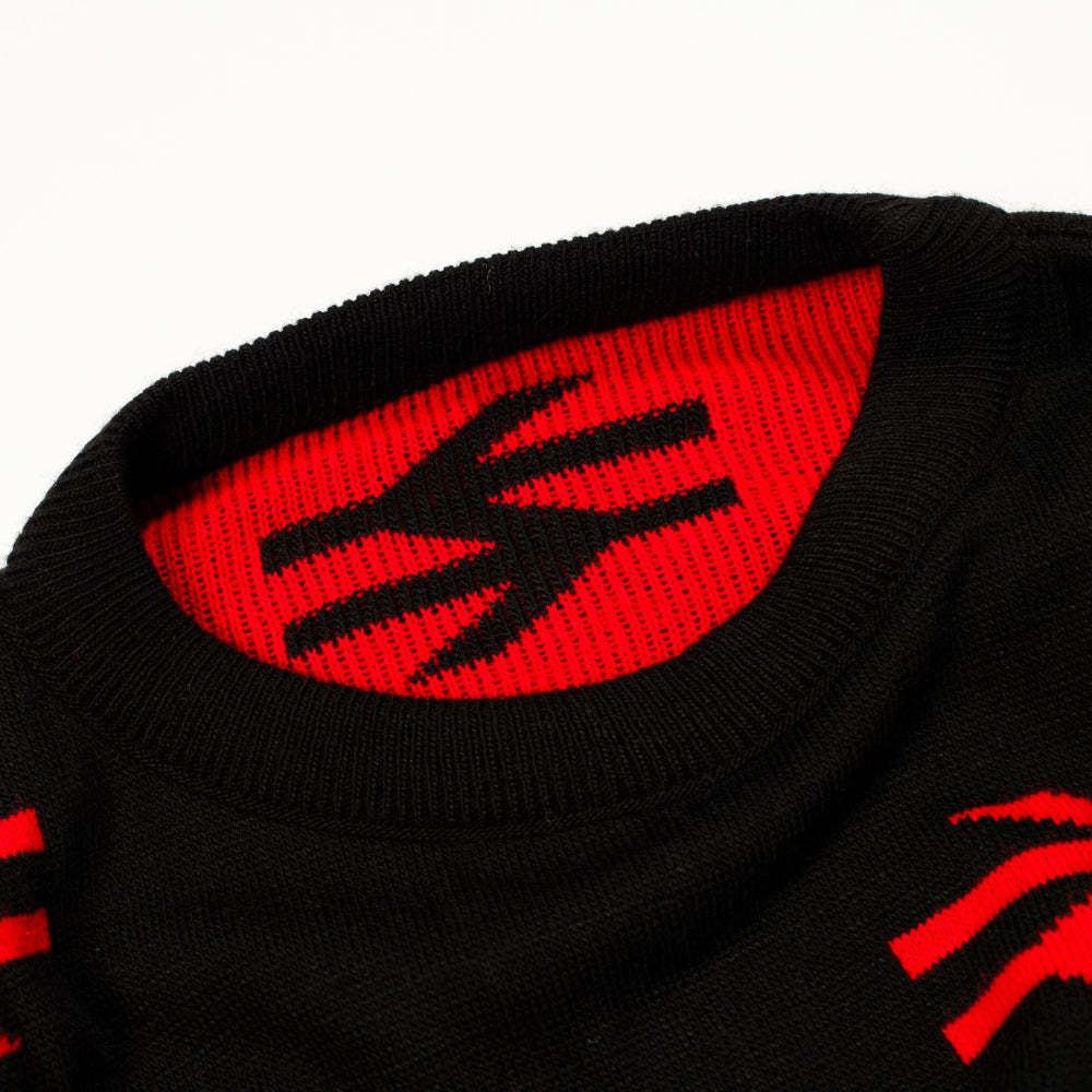 Close-up of a black knit garment, likely a sweater or hat, featuring a bold red interior collar with a black stylized logo and red knit details on the lower edge.