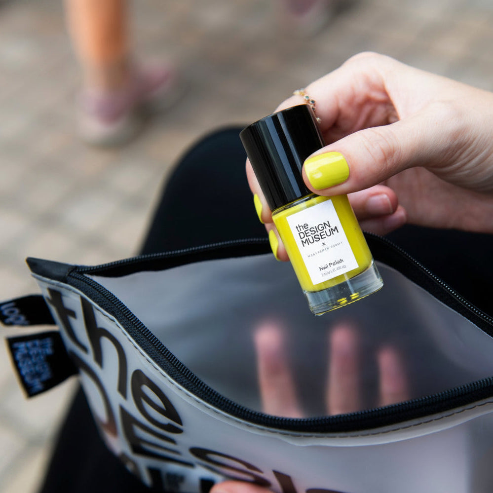 Person holding a yellow nail polish above a transparent pouch
