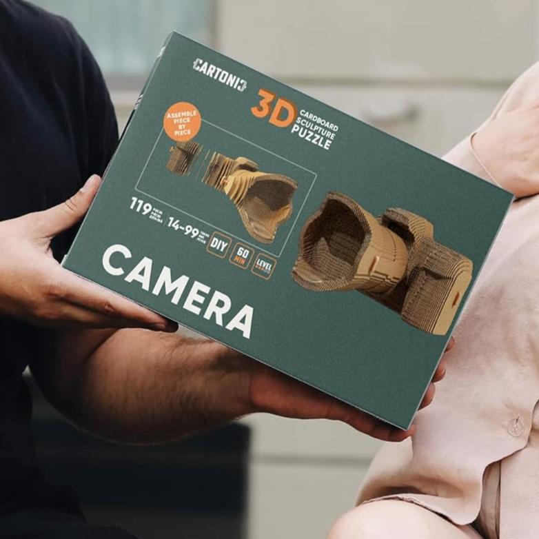 A person holding a green packaging box for a 3D cardboard model camera. 