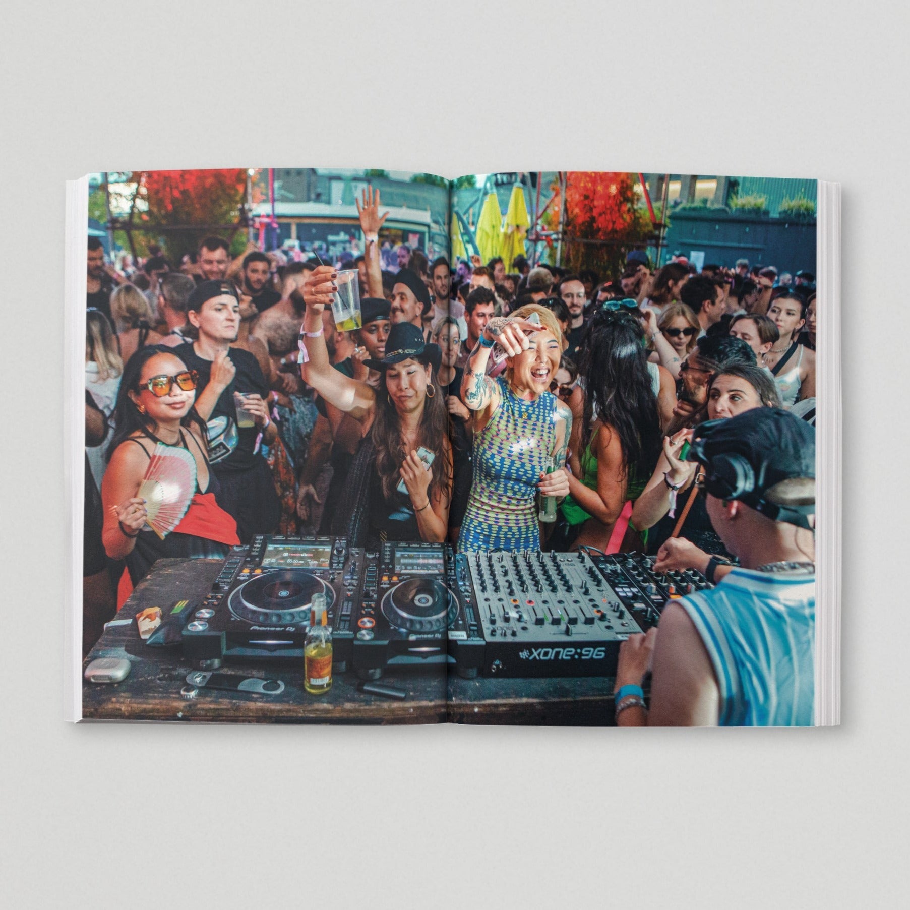 Open page of Queer London book featuring a photograph of a group of people dancing in front of some DJ decks, with a person DJing.