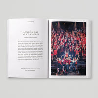 Open page of Queer London book featuring a photograph of the London Gay Men's Chorus singing  on a stage in red outfits.