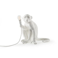 White monkey-shaped lamp holding a light bulb on a white background
