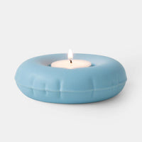 Light blue ceramic candle holder with a lit white candle on a light gray background