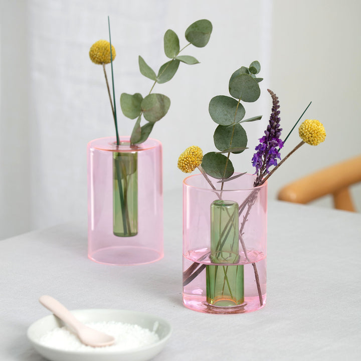 Two small reversible glass vases displayed with flowers arranged in them.