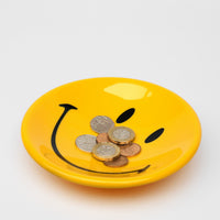 Yellow smiley face plate with coins on a white background
