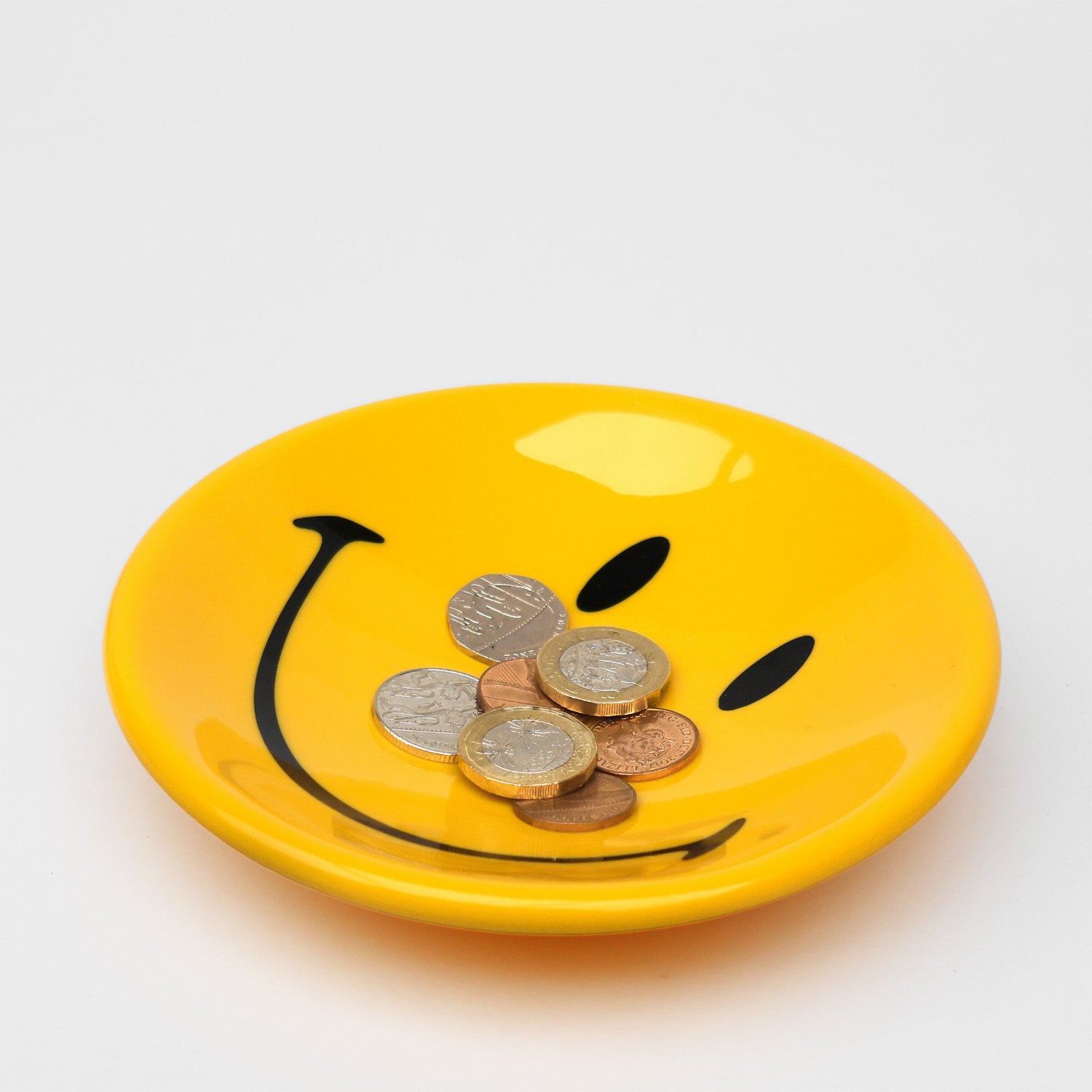 Yellow smiley face plate with coins on a white background
