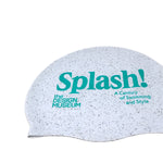 close up picture of white and grey doted swimming cap made from recycled materials featuring the Design Museum logo and the exhibition logo "Splash! A Century of Swimming and Style" on a white background

