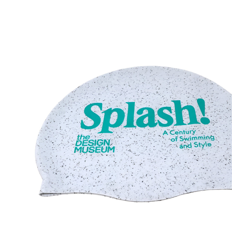 close up picture of white and grey doted swimming cap made from recycled materials featuring the Design Museum logo and the exhibition logo "Splash! A Century of Swimming and Style" on a white background
