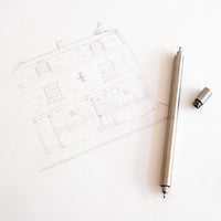 Pencil drawing of a house on paper with a pen next to it