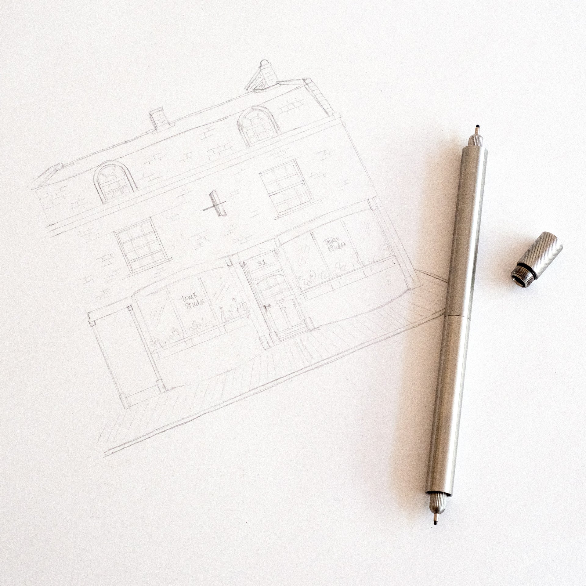 Pencil drawing of a house on paper with a pen next to it