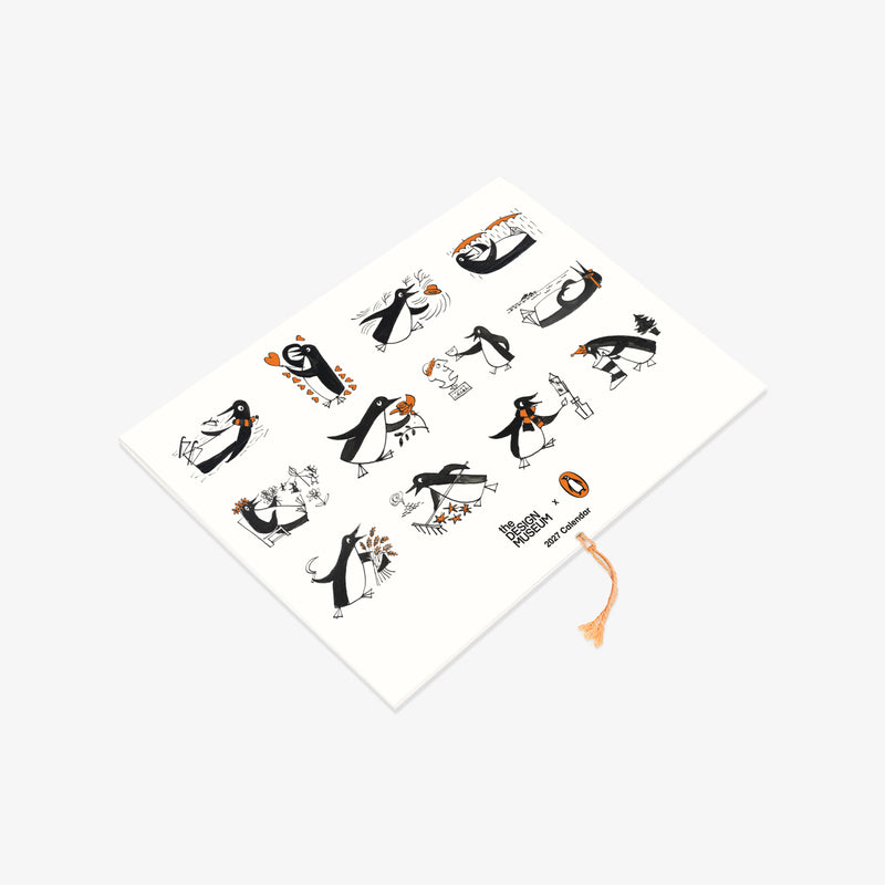 A white rectangular notebook or journal with a decorative cover featuring black and orange penguin illustrations, photographed on a light gray background.