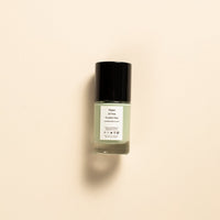 A small glass bottle of nail polish with a black cap and a white label, centered on a warm beige background.