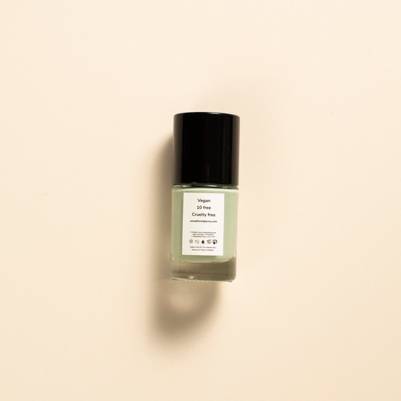 A small glass bottle of nail polish with a black cap and a white label, centered on a warm beige background.