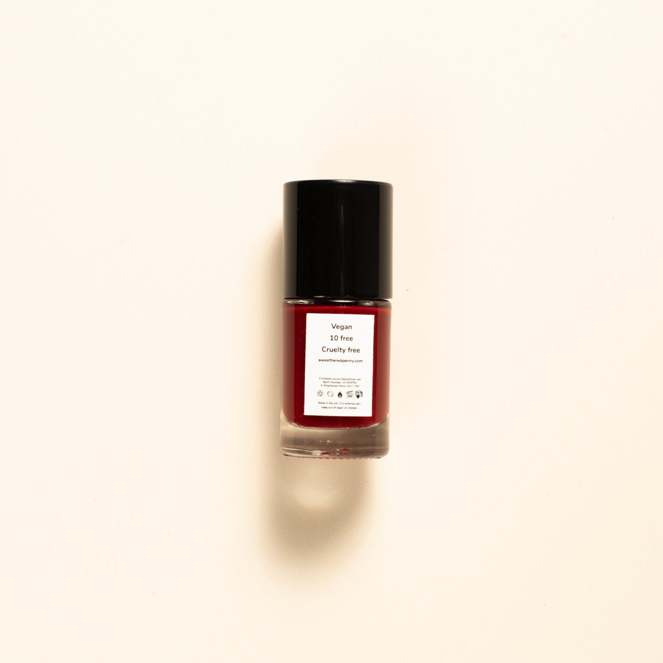 A single bottle of nail polish centered on a warm off-white background. The bottle contains a deep burgundy red polish and has a black cap with a white label.