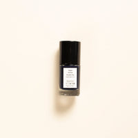 A small bottle of nail polish with a black cap and a white label, centered on a warm off-white background.