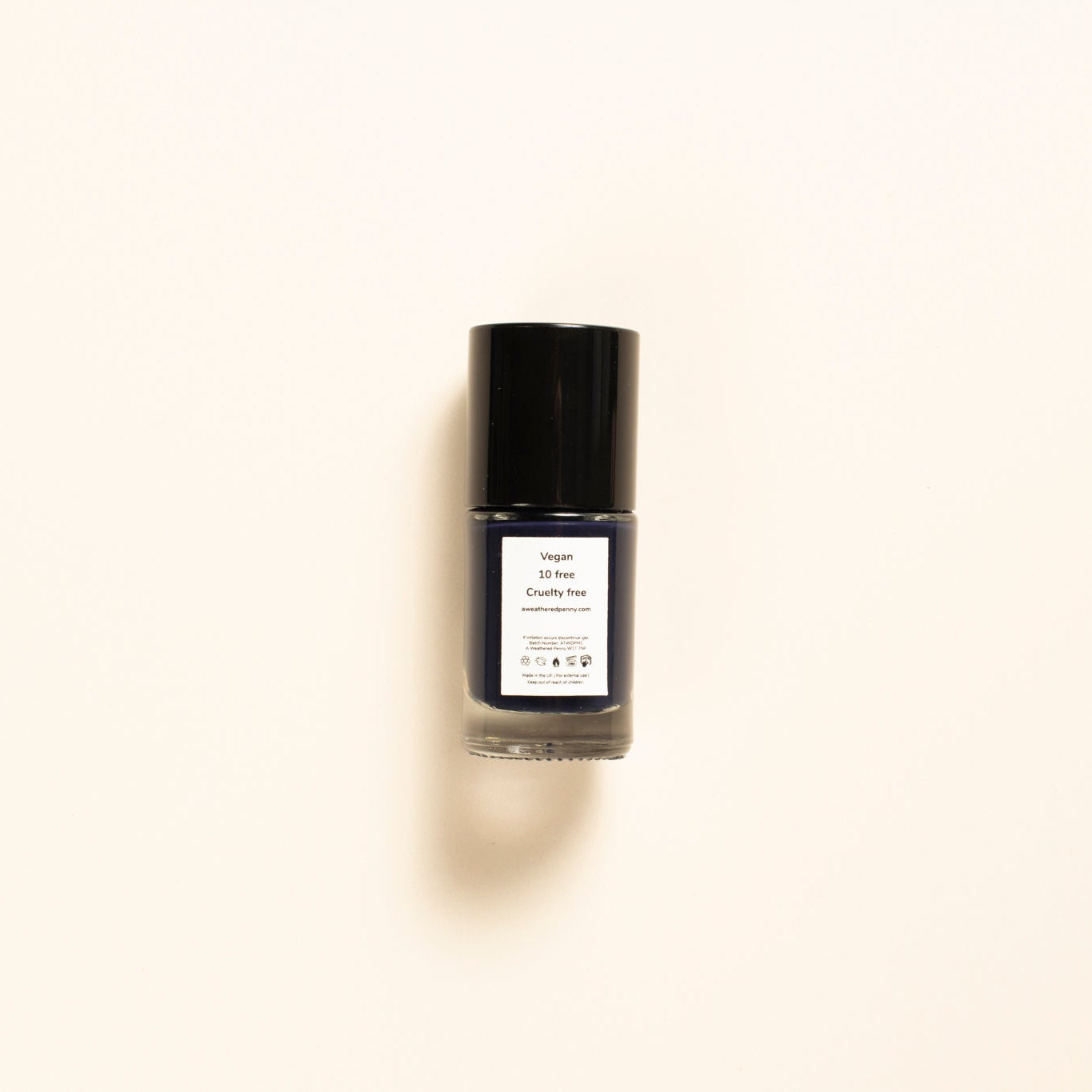 A small bottle of nail polish with a black cap and a white label, centered on a warm off-white background.
