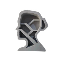 A light gray 3D model or figurine shaped like a human head profile with a staircase pattern inside, displayed on a reflective white surface.
