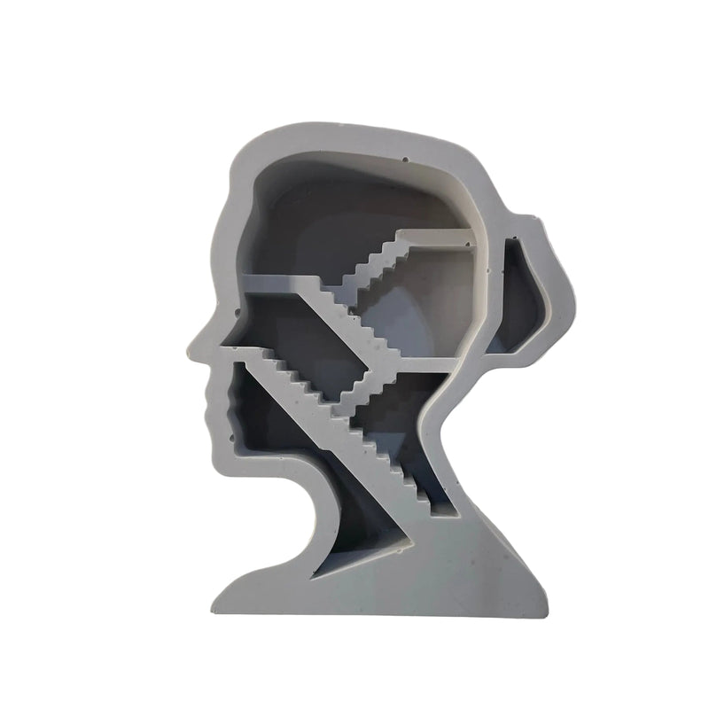 A light gray 3D model or figurine shaped like a human head profile with a staircase pattern inside, displayed on a reflective white surface.
