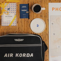 Black 'AIR KORDA' bag with a coffee cup, passport, and map on a wooden surface