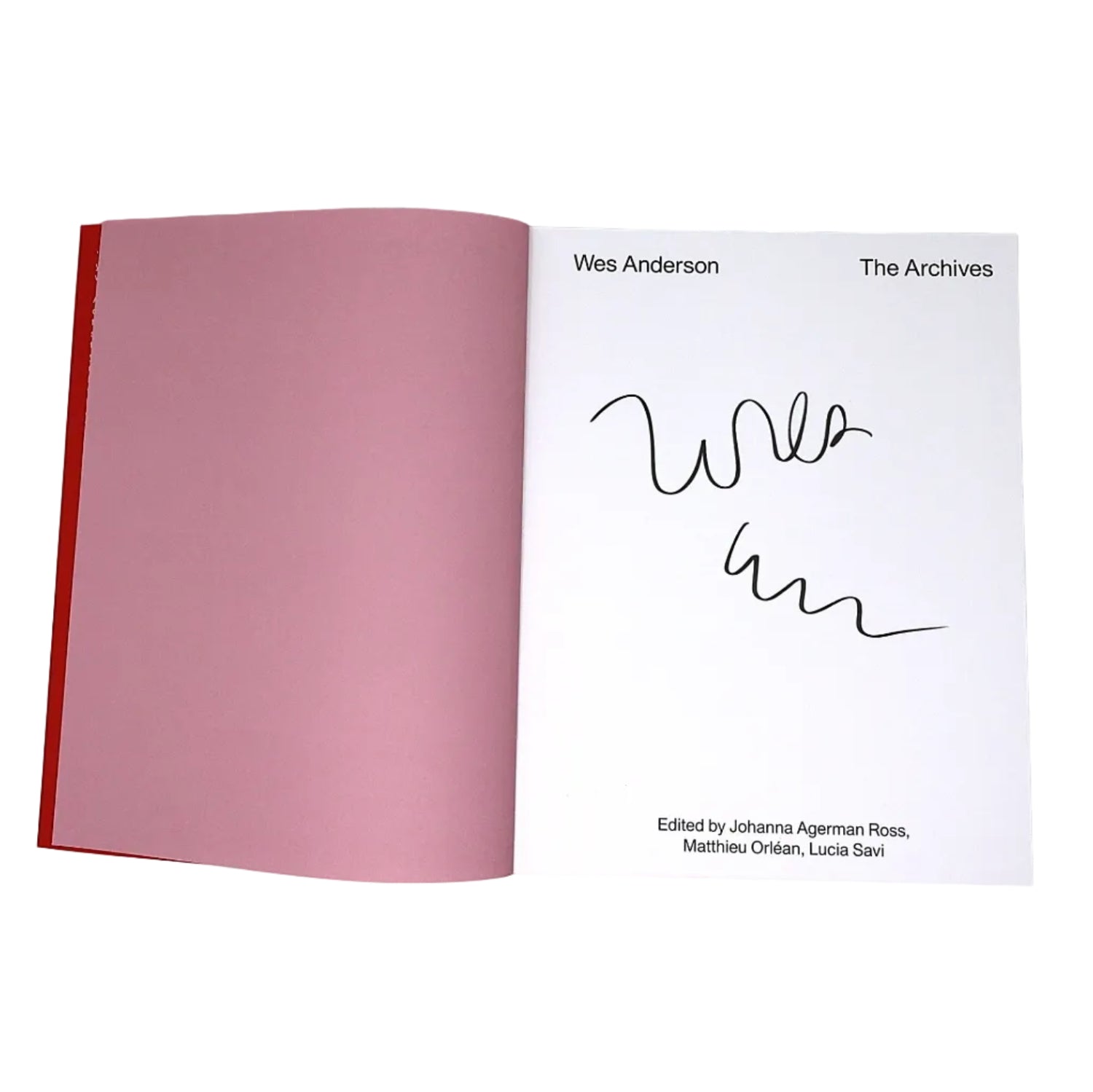 An open book or booklet showing a white page with the text 'Wes Anderson The Archives' and a black handwritten signature, alongside a large pink interior spread and a red spine edge on a white background.