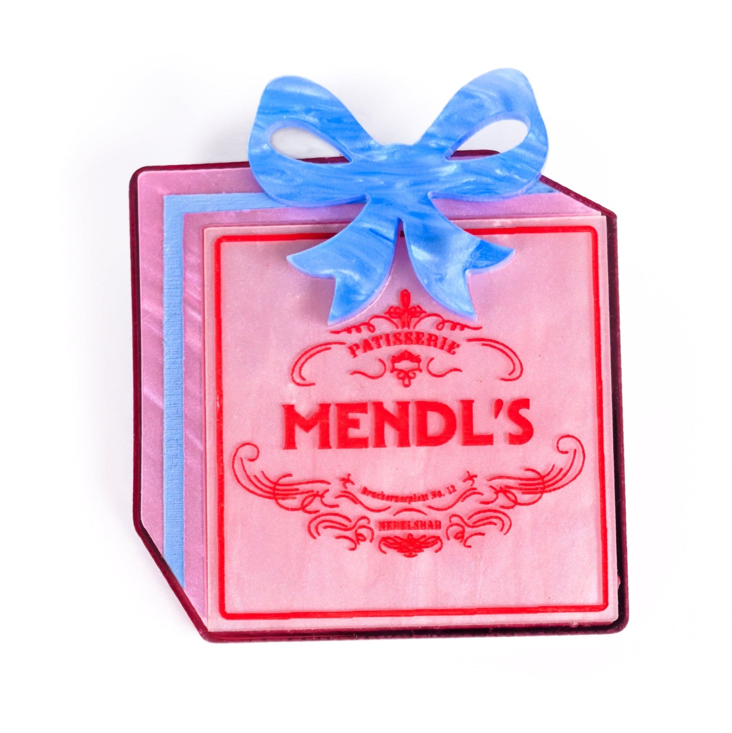Pink box brooch with blue bow and 'Mendl's' branding on a white background