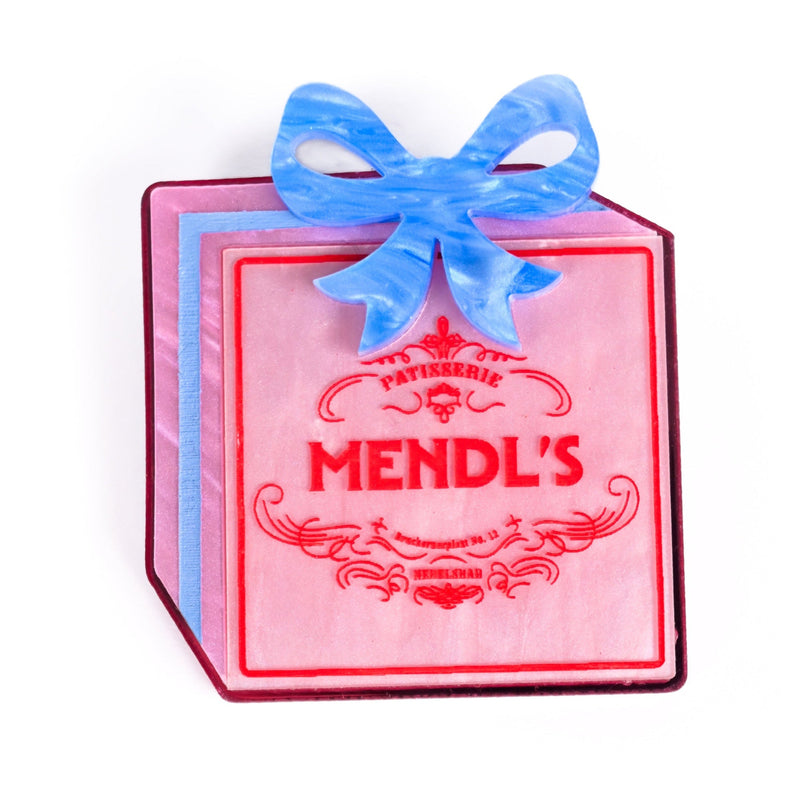 Pink box brooch with blue bow and 'Mendl's' branding on a white background