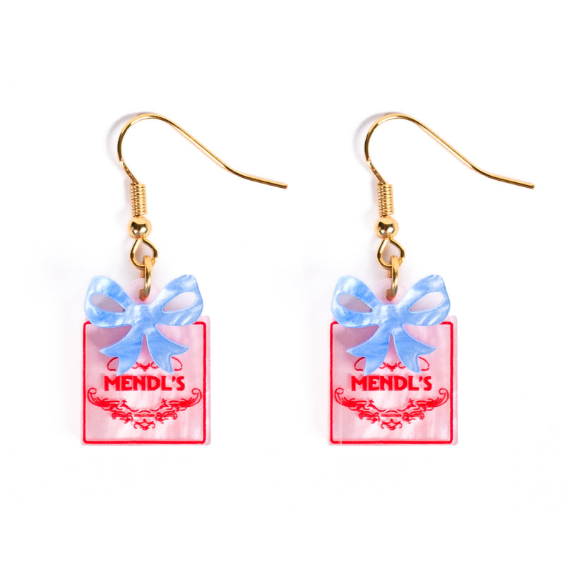 Earrings of pink boxes with blue bows labeled 'Mendl's' on a white background