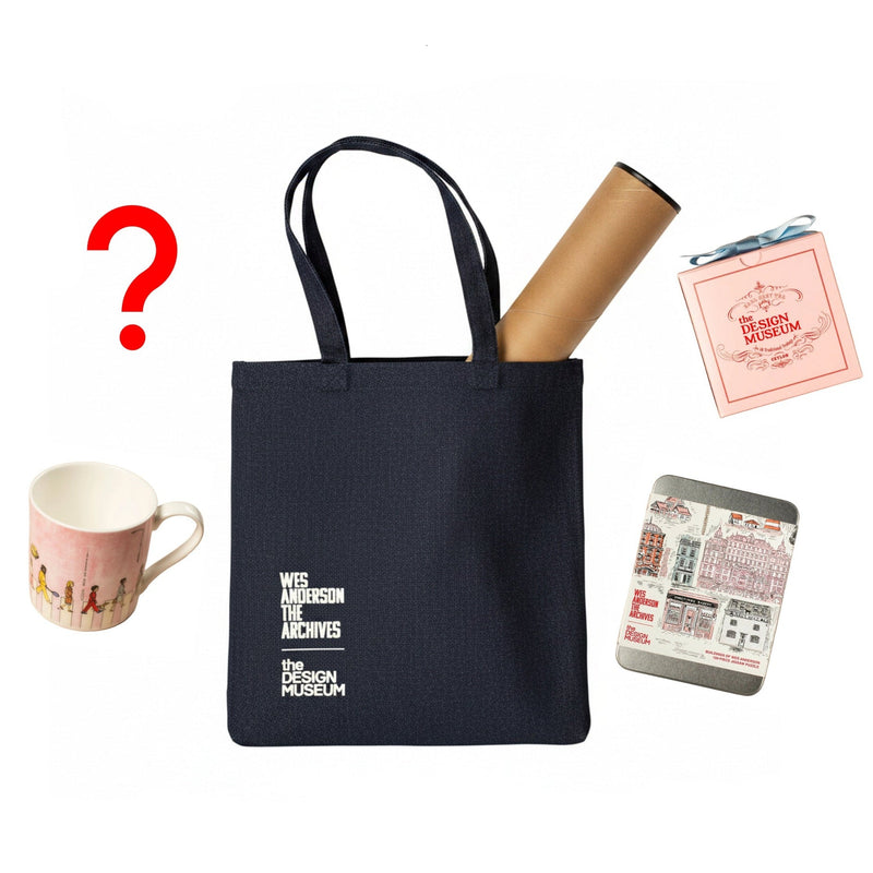 Black tote bag with 'Wes Anderson The Archives' branding, surrounded by a mug, roll of paper, and small box on a white background.