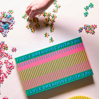 Colourful puzzle box with 'I love dreaming with you' text, surrounded by scattered puzzle pieces on a light surface.