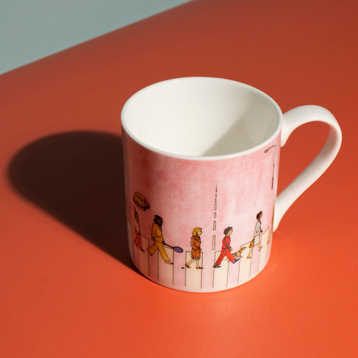 Pink mug with illustrated people walking across a crossing on an orange surface.