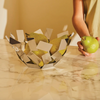 Person holding a green pear next to a decorative basket filled with pears on a marble surface.