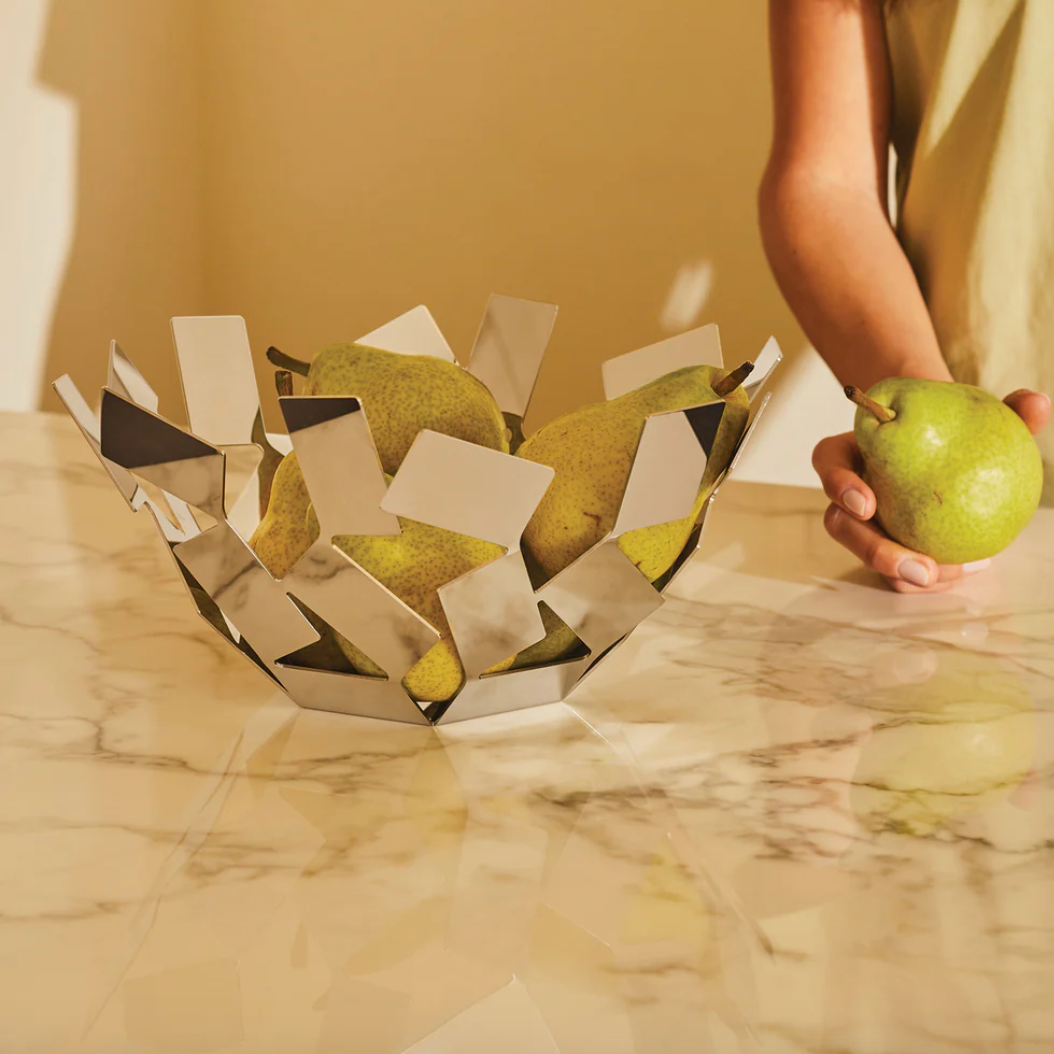 Person holding a green pear next to a decorative basket filled with pears on a marble surface.