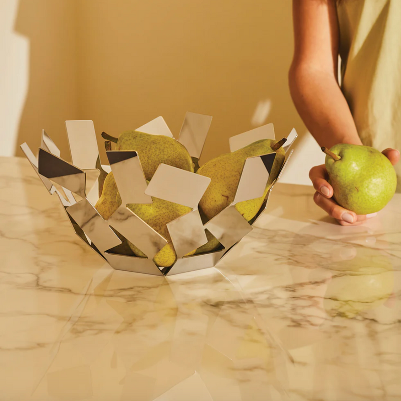 Person holding a green pear next to a decorative basket filled with pears on a marble surface.