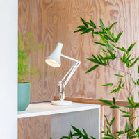 White desk lamp on a wooden surface with plants around