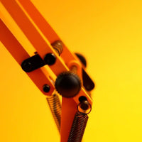Close-up of an orange metal desk lamp hinge with springs and gears on a yellow background