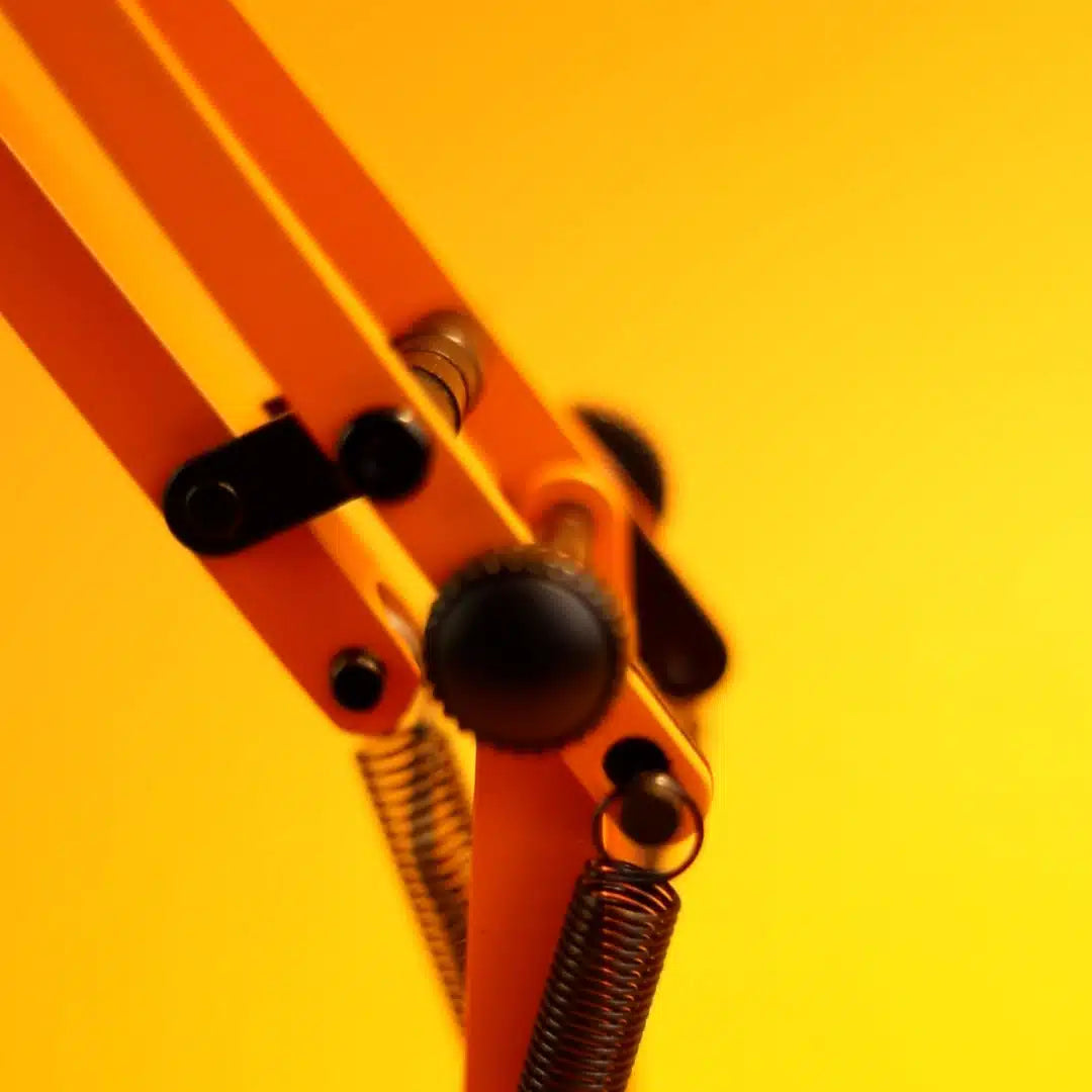 Close-up of an orange metal desk lamp hinge with springs and gears on a yellow background