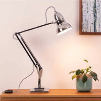 Chrome desk lamp on a wooden surface with a plant in the background