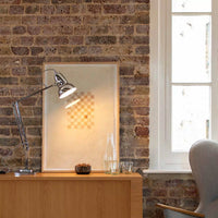 Modern interior with a wooden desk, chrome lamp, framed picture, and window on a brick wall.