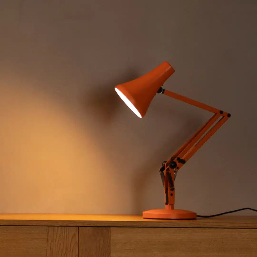 Orange desk lamp on a wooden surface with a warm glow against a neutral background