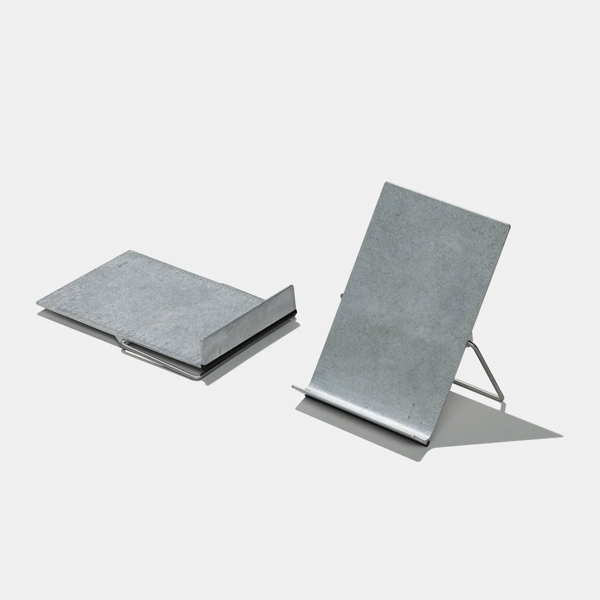 Two metal bookstands on a light gray background, one shown from a top-down view and the other from a side angle displaying its wire stand.