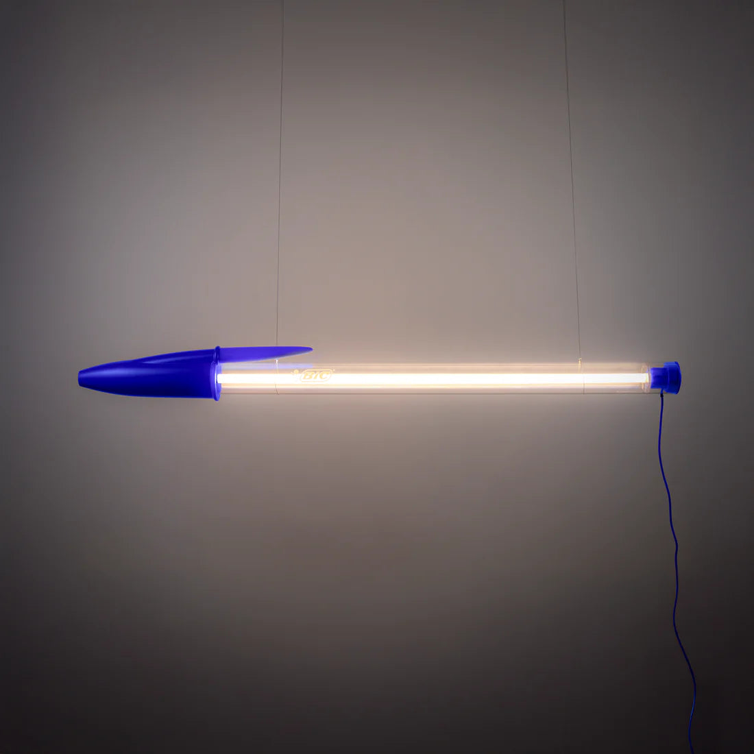 Blue BIC pen lamp hung against a grey wall. 