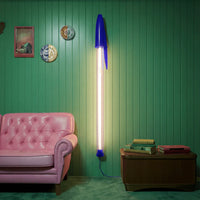 Blue BIC pen lamp on a green wall with a pink sofa and wooden cabinet.