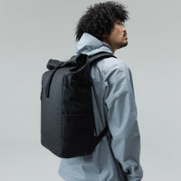 A person carrying a black backpack against a plain light gray background.