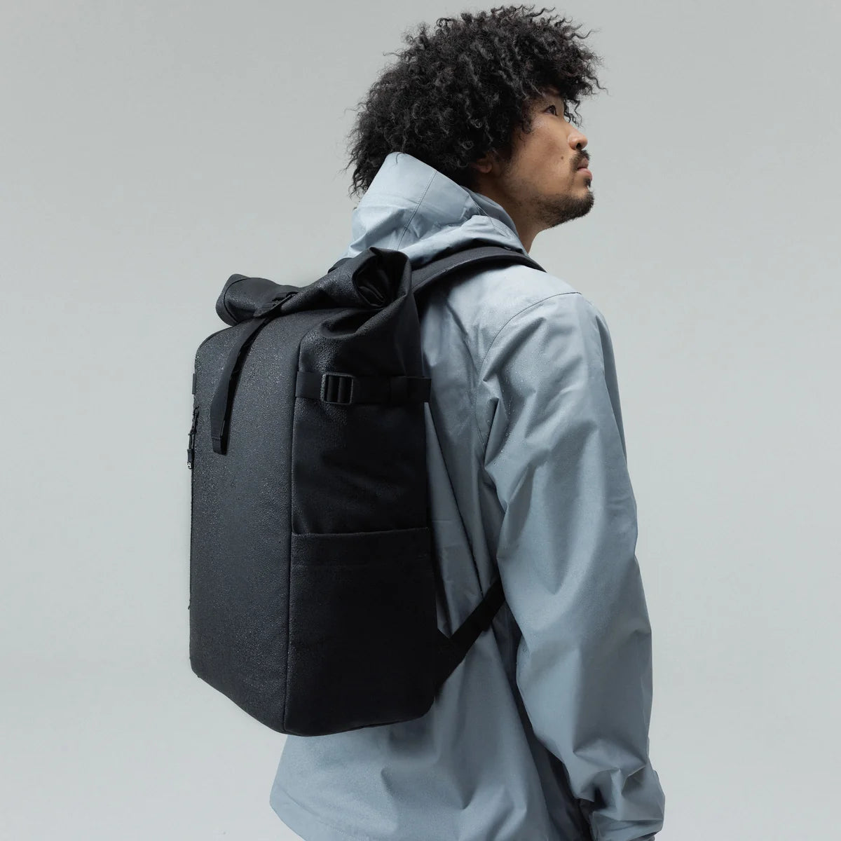 A person carrying a black backpack against a plain light gray background.