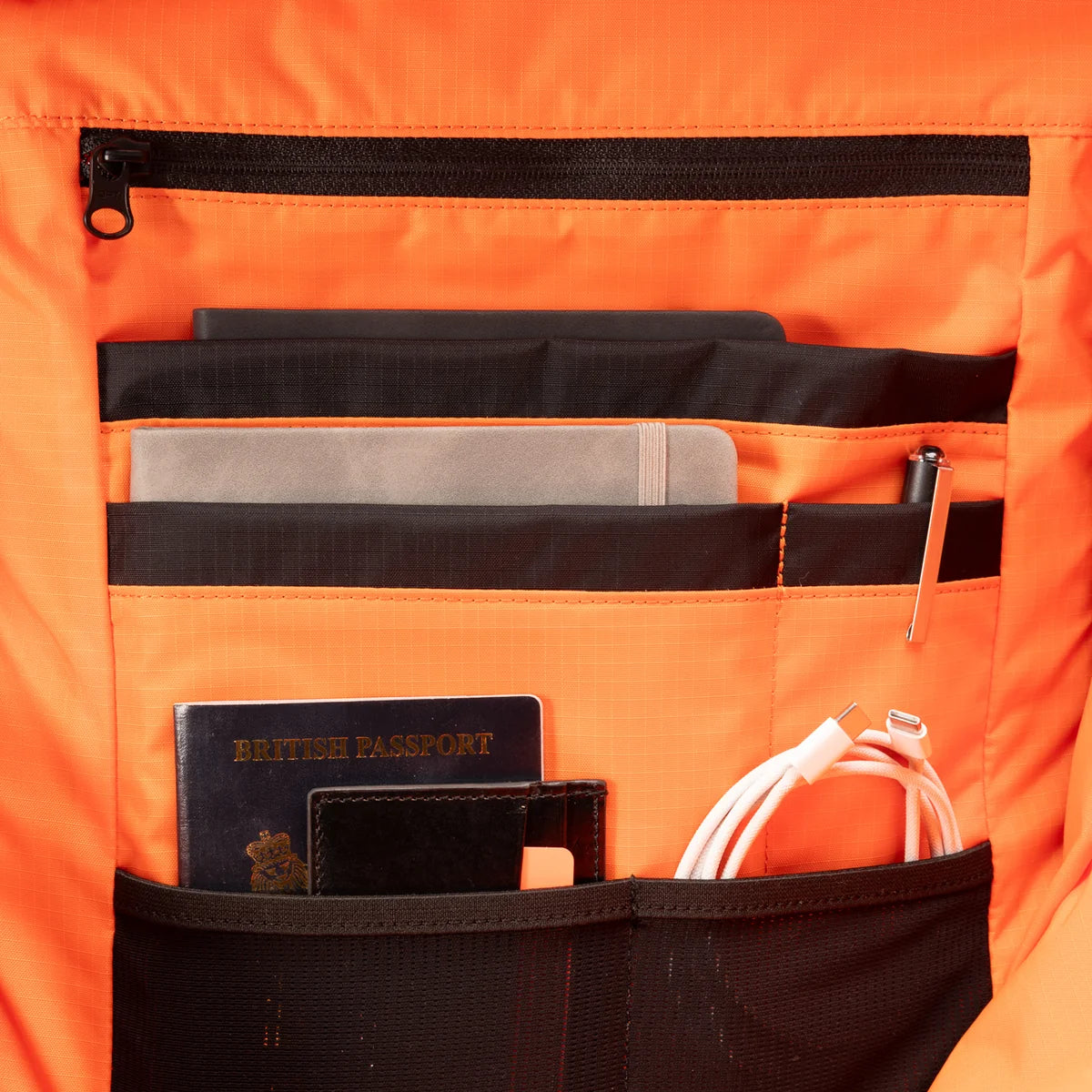 Close-up of a bright orange backpack organizer pocket holding various items in different pockets.