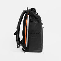 A black backpack shown from the side, with a silver laptop tucked inside a compartment against a light gray background.