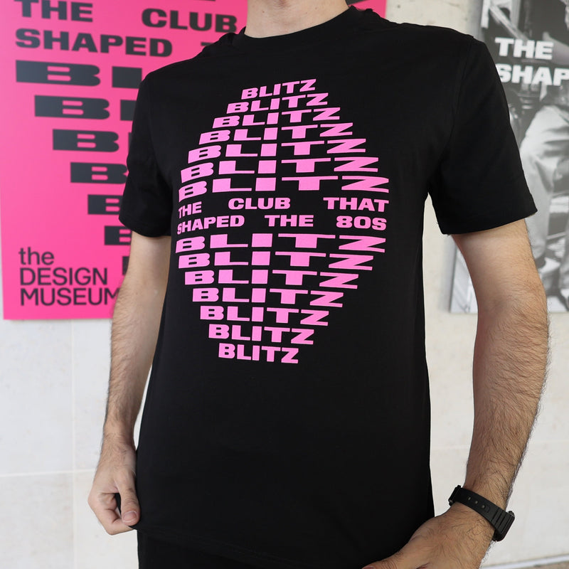 Person wearing a black t-shirt with pink text in front of a pink poster.