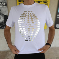 White t-shirt with gold text worn by a person, with a blurred background.