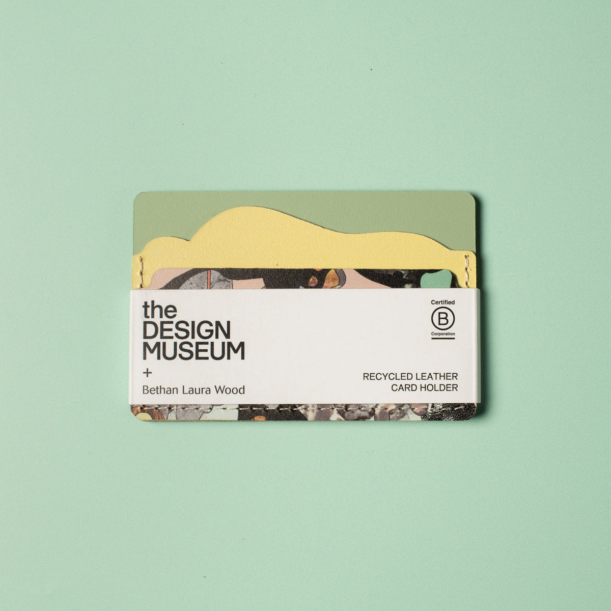 Green and yellow leather card holder with white packaging strip on a light green background